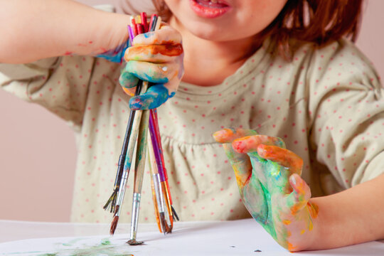 A child holding paintbrushes with colorful hands &mdash; a symbol of early creative freedom.