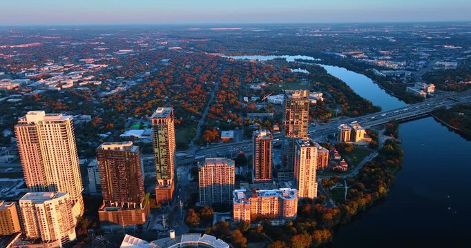 Diverse high-rise buildings at the green waterfront of the Colorado River. Approaching a wide-lane highway with hectic traffic on it. Austin, Texas, USA.