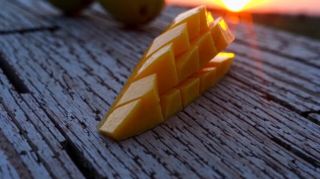 Golden mango slices are artistically arranged on a rustic wooden surface, reflecting the warm rays of the setting sun. The vibrant mango slices and the textured wood create a relaxed atmosphere.
