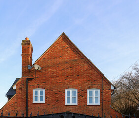 Red brick dwelling showing chimney, windows, and roofline against a clear sky, representing home and residential living