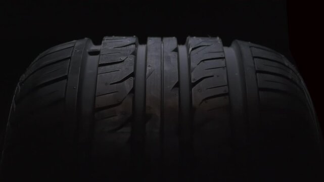 Slow Forward Motion of a Wheel. The new car tire is highlighted by a spotlight in the dark. The wheel rotates slowly toward the viewer against a black background