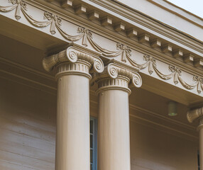 Close up of ornate neoclassical building facade with Ionic columns and sculpted decorations.