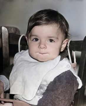 Vintage portrait of a one year old girl eating. The child's mouth is in porridge. Retro photo from 1995.