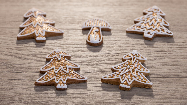 Closeup golden baked gingerbread cookies decorated by white icing on wood background. Group of traditional Christmas or New Year sweets in tree or mushroom shape with beautiful winter snow decoration.