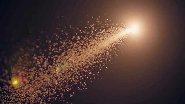 The bright light emits a sparkling trail of particles, creating an enchanting scene in the dark atmosphere. This captivating light display mesmerizes viewers with its shimmering particles and glow.