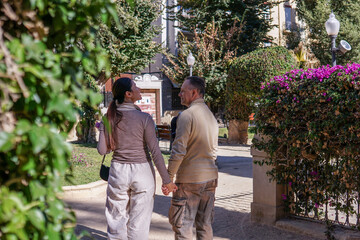 mature couple in a sunny park. The 50-year-old man gives flowers to his 40-year-old partner. They smile and enjoy a romantic moment outdoors with greenery and trees.
