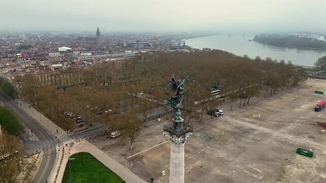 Drone shot of bronze angel statue on Monument aux Girondins overlooking misty Bordeaux, empty Quinconces square and river