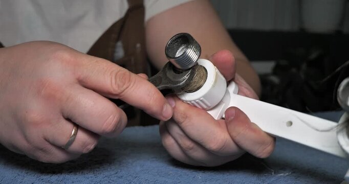 A professional plumber uses a wrench to tighten a threaded fitting coated with sealant. A plumber ensures a secure and watertight connection when installing or repairing a home's plumbing system.