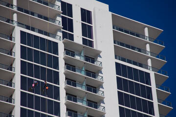 Modern High-Rise Building With Glass Facade And Rappelling Window cleaners Workers On A Clear Day in St. Petersburg, FL. Expansive glass panels and stacked balconies. Two workers in safety gear descen