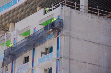 Construction Workers in safety gear Install Exterior Facade Using Suspended Safety Net Scaffolding on Building Under Construction Site in St. Petersburg, FL. Partially built building, showcasing teamw