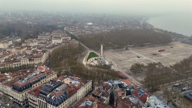 Drone shot of Bordeaux historic center with Monument aux Girondins column, tree-lined esplanade and Garonne river waterfront