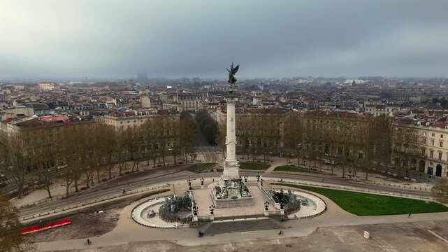 Drone shot of Monument aux Girondins angel statue on Esplanade des Quinconces framed by trees and historic city buildings
