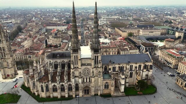 Drone video of Saint-Andre Cathedral and Pey Berland Tower rising above dense tiled rooftops in historic Bordeaux under a moody overcast sky
