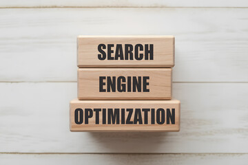Top-down flat lay of three light wooden blocks stacked with bold text SEARCH, ENGINE, OPTIMIZATION on a white plank background. Minimalist, professional aesthetic.