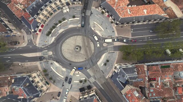 Top down drone shot of dynamic busy roundabout with tram lines and cars in Bordeaux France forming geometric pattern