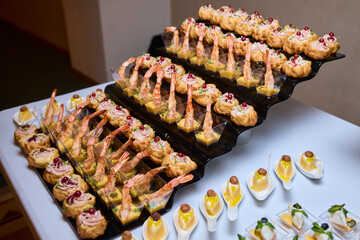 Elegant dining presentation, Sophisticated arrangement of canapes on stylish table setting, Exquisite black trays with gourmet delicacies showcased in upscale event ambiance