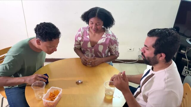 Three young multicultural friends having fun, laughing, and playing a guessing game at a table