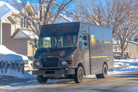 Calgary, Alberta, Canada. Dec 12, 2025. A brown UPS "Worldwide Services" delivery truck is parked on a slushy, snow-covered residential street, delivering packages during winter.