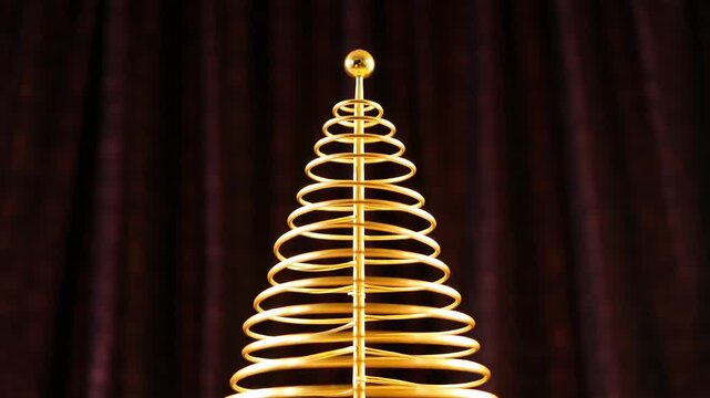 Close up vertical shot of a modern, minimal golden metal wire spring shaped like a christmas tree with a small ball on top