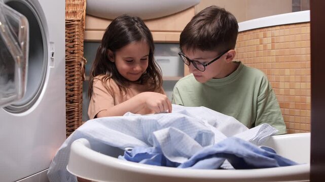 Children learning responsibility by helping with household chores, loading and unloading clothes from the washing machine, fostering teamwork and family bonding in the bathroom