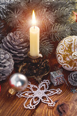 Burning candle for Christmas Eve holiday. Branch of christmas tree with balls and decorations on old barn wood background.