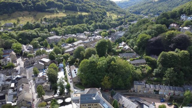 aerial drone view of Hebden Bridge town centre showing the shops and houses surrounding the river and bridge and valley landscape in summer
