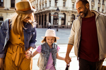 Adult parents holding hands with happy daughter on city street
