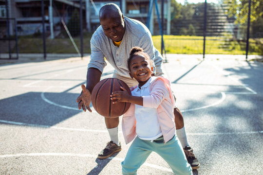 Grandfather teaching happy child granddaughter basketball on outdoor court