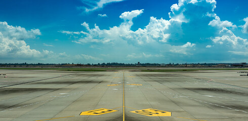 Wide empty airport runway and taxiway under a bright blue sky
