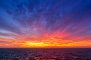 Epic ocean sunset seascape with purple blue storm clouds and golden hour fire over calm open water horizon serene coastal landscape photography fine art wall print for travel dreamers at dusk today