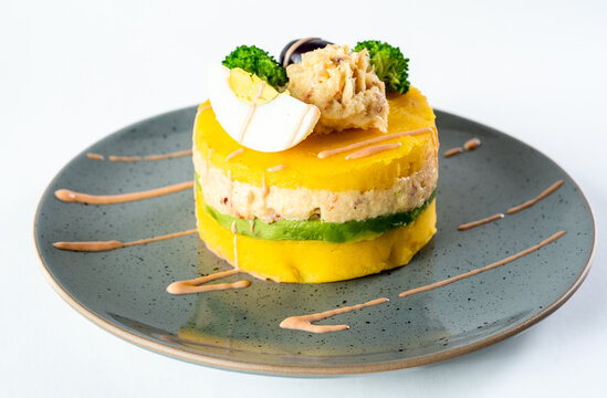 PERUVIAN FOOD. Causa rellena de pollo. Chicken causa rellena. Traditional peruvian dish from yellow potato, chicken, avocado on white plate.