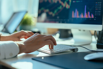 Closeup of hands typing on a keyboard in front of a computer displaying financial market data