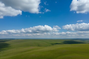 Obraz premium Expansive green rolling hills under a bright blue sky with white clouds