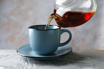 Pouring hot tea into cup from teapot at grey table, closeup