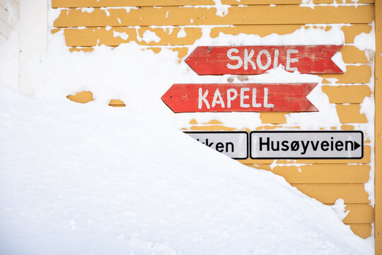 Red street signs against a yellow wall in Husoy, Norway