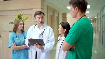 Medical team discussing patient data on tablet in hospital hallway. - Powered by Adobe