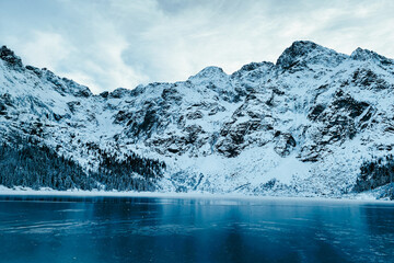 Snow-covered Morskie Oko lake surrounded by mountains and pine forest in Zakopane, Poland. Winter alpine landscape with frozen water and dramatic peaks © shustrilka