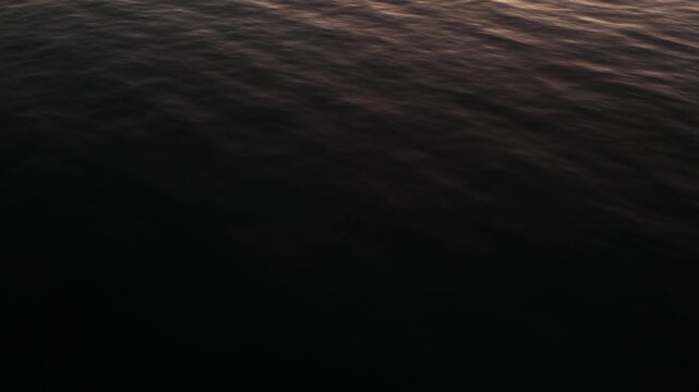 Minimalist dark water background showing the subtle movement of the sea surface in low light conditions captured by a drone for abstract video projects