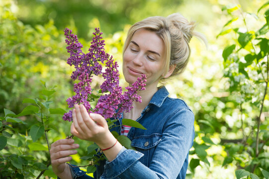 A woman smells lilacs on a branch in the garden