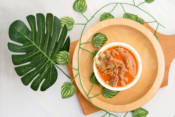 Rich Indonesian goat curry (Gulai Kambing) in a white bowl, served on a light wooden platter, featuring tender meat, bones, and a creamy, spicy coconut milk broth