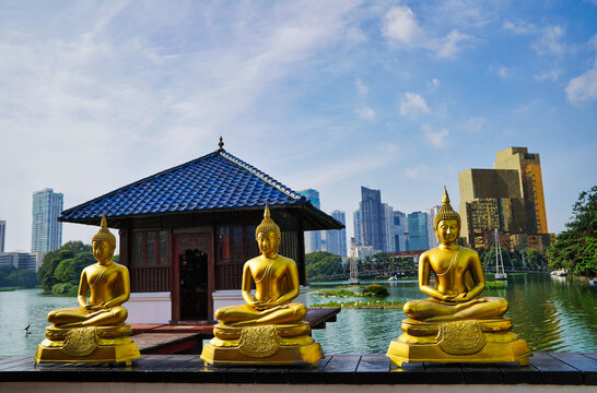 Serene Gilded Buddhas statues in meditation in contrast with the modern city skyline of Colombo at the picturesque Seema Malaka temple,Beira Lake,by architect Geoffrey Bawa,1976 in Colombo,Sri Lanka