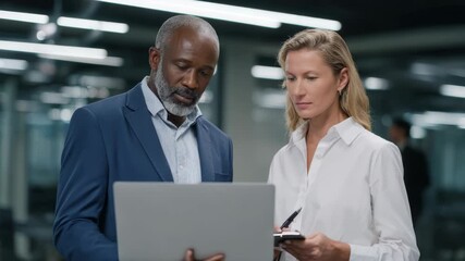 Diverse business team collaborating, reviewing data on laptop in office - Powered by Adobe