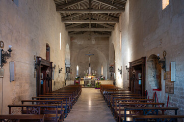 The austere Romanesque interior of the Pieve di San Giusto in Suvereto, Tuscany, featuring a single nave, rough stone walls, a visible timber roof structure, and a central altar illuminated by natural