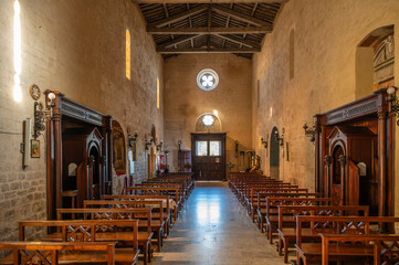 The severe Romanesque interior of Pieve di San Giusto, Suvereto. The central nave features a visible timber roof structure, rough stone walls, and light filtering through the small rose window
