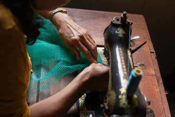 Close up hands using a vintage sewing machine to sew green mesh fabric. Concept of traditional craft and meticulous manual labor