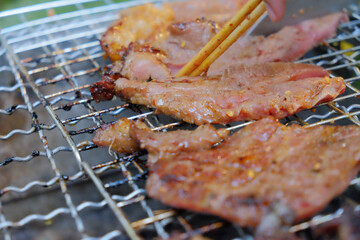 Close-up of chopsticks turning marinated meat slices on a hot grill