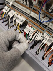 Gloved Hand Holding Labeled White Wire in Electrical Terminal Panel