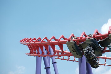 Suspended roller coaster car rounding a turn against a blue sky