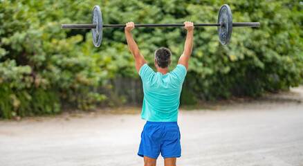 Man exercising with barbell outdoor, back view. Man athlete lifting barbell. Strong man do sport exercise. Gym workout. Sport athlete man with barbell. Healthy lifestyle barbell training