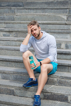 Sport runner man having thirst. Healthy lifestyle. Water balance in body. Sport man feel thirst drinking water. Thirsty runner relax at stairs after workout. Tired thirsty man hold water